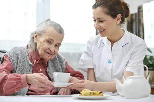 Betreuerin unterstützt eine lächelnde Seniorin liebevoll im Alltag zu Hause